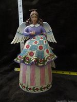 Front view of Jim Shore angel quilting figurine showing detailed multicolor dress and wings with measuring tape for scale