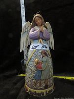 Front view of 9-inch Jim Shore angel figurine with decorative skirt and wings against black background with measuring tape