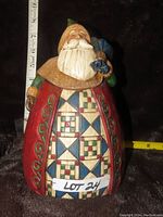 Front view of the Jim Shore Santa figurine showing detailed patchwork quilt robe with red, blue, green, and cream colors, holding a blue bag, measuring about 8 inches tall.
