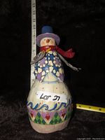 Photo showing the front of the snowman figurine standing against a black background with measuring tape indicating height approximately 9 inches.