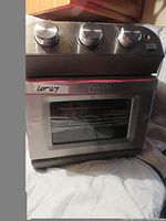 Dash 10-liter air fryer oven with stainless steel front and three control knobs, new condition, in red color.