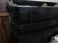 Stacked black plastic storage bins with visible reinforced side handles and shape for stacking.