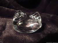 Front side view of the clear glass hen-shaped handcooler on a textured dark fabric.