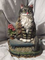 Front view of the hand painted cast iron cat door stop showing the cat sitting on a bench with flower pot detail.