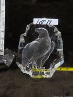 Front view of the crystal glass block showing the engraved eagle sculpture inside with detailed feathers and claws, ruler for size reference.