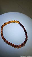Stretchy Baltic amber bracelet with small round beads, showing a smooth gradient from light honey to dark reddish-brown amber colors.