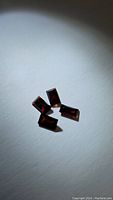 Five deep red garnet stones arranged loosely on a gray surface with shadowing, showing their fancy baguette cuts and rectangular shapes.