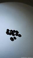 A photo showing multiple small polished round jet black onyx cabochon gemstones grouped on a white background.