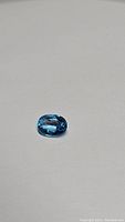 Image showing oval cut blue zircon gemstone on neutral background, highlighting the clarity and blue color.