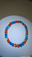 Photo of circular stretchy bracelet with round polished agate beads in blue and red hues on white background.