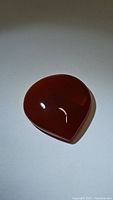 Full view of the teardrop-shaped deep orange-red carnelian gemstone on a plain background showing its polished smooth surface.