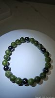 Image of natural green jade and hematite beaded bracelet on white surface, shows alternating bead pattern and elastic stretch cord.