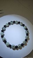 Top view of stretchy gemstone bead bracelet showing alternating light green kiwi jasper and black onyx beads arranged in a circle on white background.