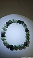 Photo of stretchy bracelet with alternating natural green spotted jasper and black lava stone beads, 8mm size, circular arrangement on neutral background.