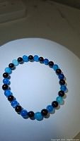 Natural ocean blue agate and jet black onyx round polished beads stretchy bracelet laid flat on a white surface, showing color and bead size.