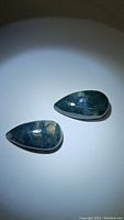 Image showing two polished pear-shaped moss agate cabochons with visible green moss-like inclusions.