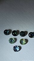 Seven natural round cut sapphires in various blue-green shades, arranged on a textured white background.