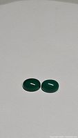 Two oval vivid green cabochon cut onyx gemstones placed on a flat light surface showing translucent green color.