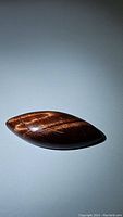 Natural red tiger's eye marquis-shaped cabochon gemstone photographed with visible flash effect on polished surface.