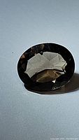 Photo of an oval cut natural smokey quartz gemstone showing faceting and color on a plain background.