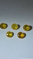 Five round cut yellow sapphire gemstones evenly spaced on a flat surface under white lighting, showing clear bright yellow coloration and transparency.