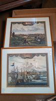 Two framed antique/vintage colored engravings featuring maritime scenes with sailing ships and coastal city views, placed on the floor