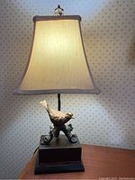 Photo of the whole lamp lit showing fabric shade and wooden base with bird figurine
