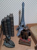Photo showing the Eiffel Tower metal bookend, stack of vintage books, owl figurine on books, and mouse figurine on leaf, arranged on a surface against patterned wallpaper.
