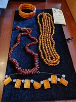 Full view of five amber jewelry pieces including bracelets, necklaces and hatpin on black cloth