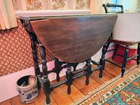 Side view of an oval wooden drop leaf table showing one leaf raised and the turned legs and stretchers.