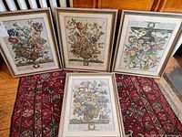Four framed floral prints displayed together on a patterned rug, showing the full set and their frames.