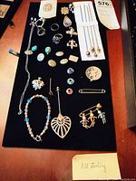Wide shot of lot on black felt showing all jewelry pieces arranged for display, with notes indicating mostly sterling silver content.