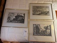 Top view of three framed black and white etching prints laid out on a bed showing different architectural scenes.