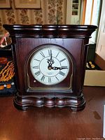 Front view of Seiko wooden mantel clock with Roman numeral face and decorative wood base.