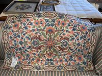 Full view of vintage crewel needlepoint wall hanging on striped couch, showing overall floral design and border.