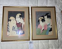 Two framed wood block prints showing Japanese men, each double matted and hung in gold-toned frames, laid side by side on a bed.