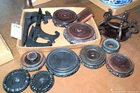 Multiple wooden stands in various sizes and styles including carved round bases and easel stands on a flat surface with some dust.