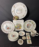 Photo of full Beatrix Potter collectibles lot including plates, mug, decorative tiles, bowls, cookbook, and basket of miniature vegetables.