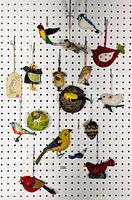 17 assorted bird ornaments hanging on pegboard backdrop in various colors and styles, sizes range 2" to 4".