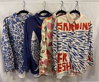 Four bright quarter-button dress shirts hanging on black hangers, showing different colorful designs including fish, botanical, and fruit motifs.