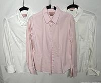 Three Pink of London blouses on hangers, two white and one pink blouse in the center.