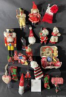 Photo showing a collection of Christmas ornaments including a large wooden nutcracker, miniature Santa figures, knitted hats, stockings, and other festive ornaments arranged on a black background.