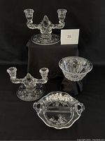 Photo showing two etched glass candlesticks, a small etched glass bowl, and a two-part serving bowl with silver overlay on black backdrop.