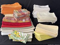 Photo showing stacks of various colored tablecloths and napkins, including orange, red, beige, white cloths and patterned napkins.