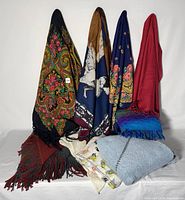 Overall group of 9 assorted wool and blended scarves displayed hanging and folded, showing variety of colors and patterns.