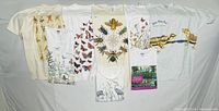 Photo showing eight nature-inspired tee shirts laid out flat with visible large prints featuring bees, butterflies, birds, frogs, flowers and a garden photo
