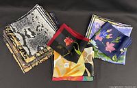 Nine assorted silk scarves folded and stacked showing various prints and colors including animal, floral, and abstract designs.
