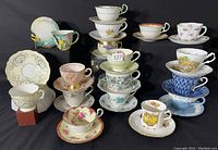 Group photo of all 17 assorted teacups stacked on matching saucers with various floral and decorative patterns in pastel and vivid colors.
