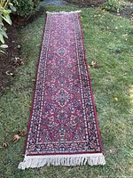 Full view of the Karastan Red Sarouk runner rug laid on grass, showing the red floral pattern and borders with fringed end.