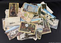Image of a pile of over 140 vintage postcards showing varied subjects such as urban buildings, large redwood trees, seascapes, white birds, and colorful clock faces.